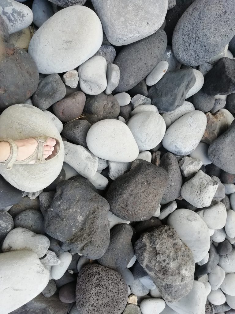 A feet in sandal standing on a field of rocks of the size of a melon.